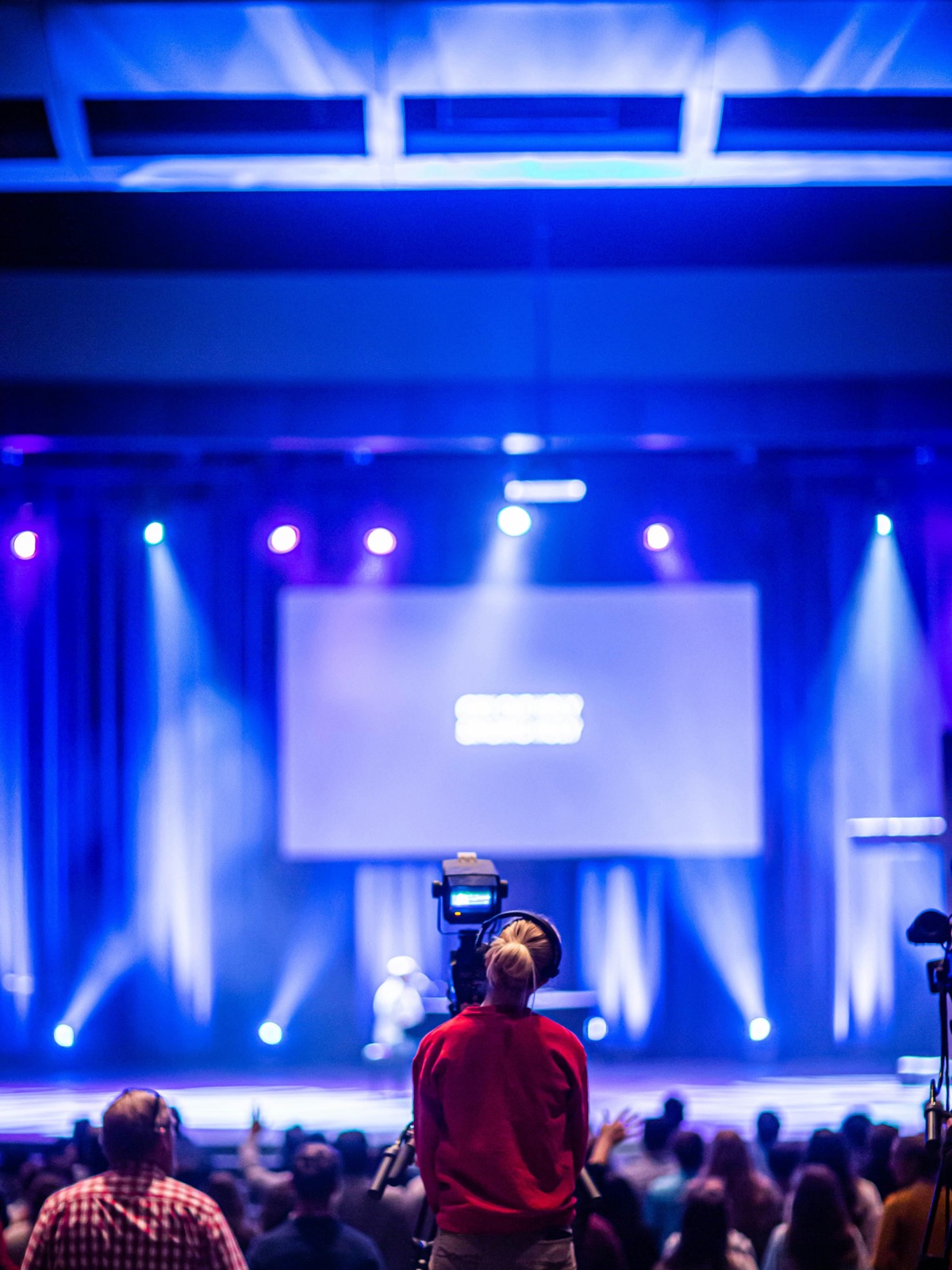 A camera operator captures footage of a stage event with blue production lighting