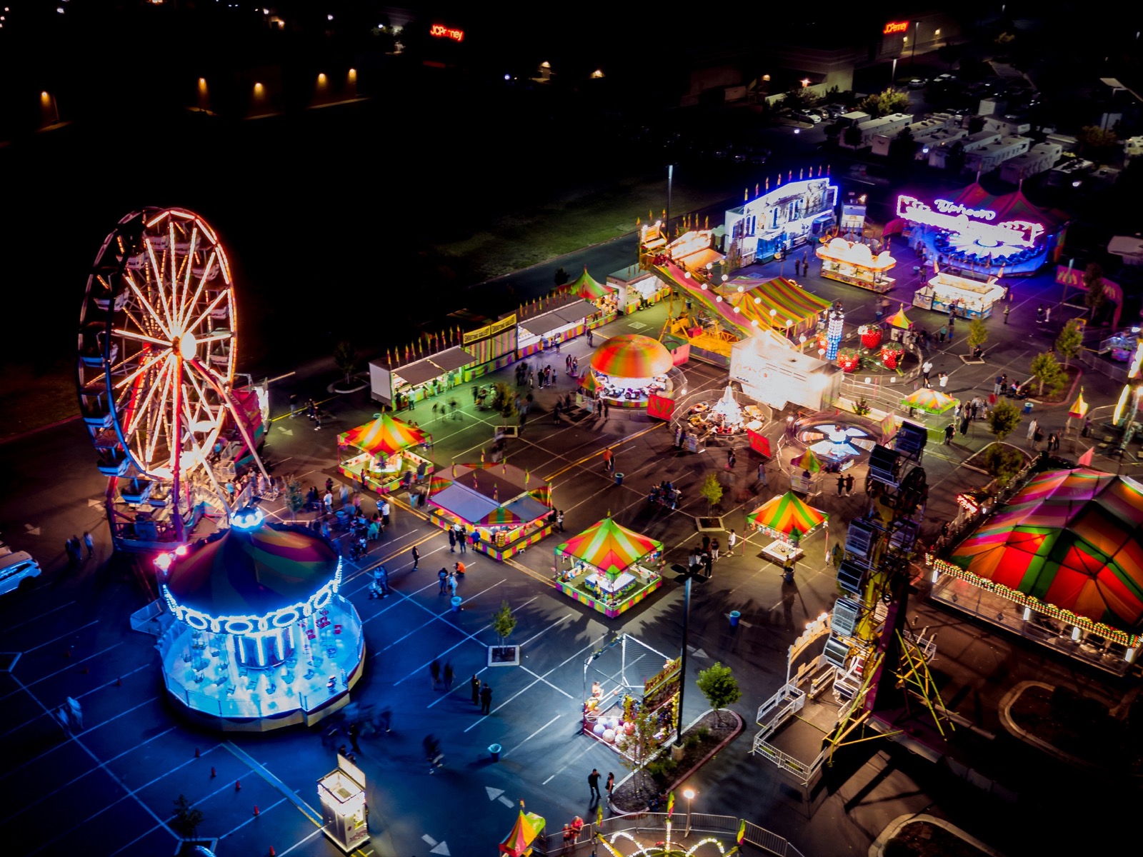 Aerial view of an illuminated outdoor fair at night with Ferris wheel, carnival rides, and lit tents